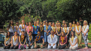 Teilnehmende einer Yogalehrer-Ausbildung üben Korrekturen zu zweit in einer Ashram-Halle in Rishikesh